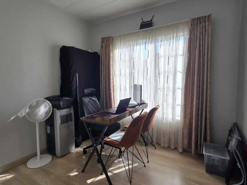 A functional bedroom space featuring laminate flooring and large windows with curtain treatments, currently utilized as a home office area.