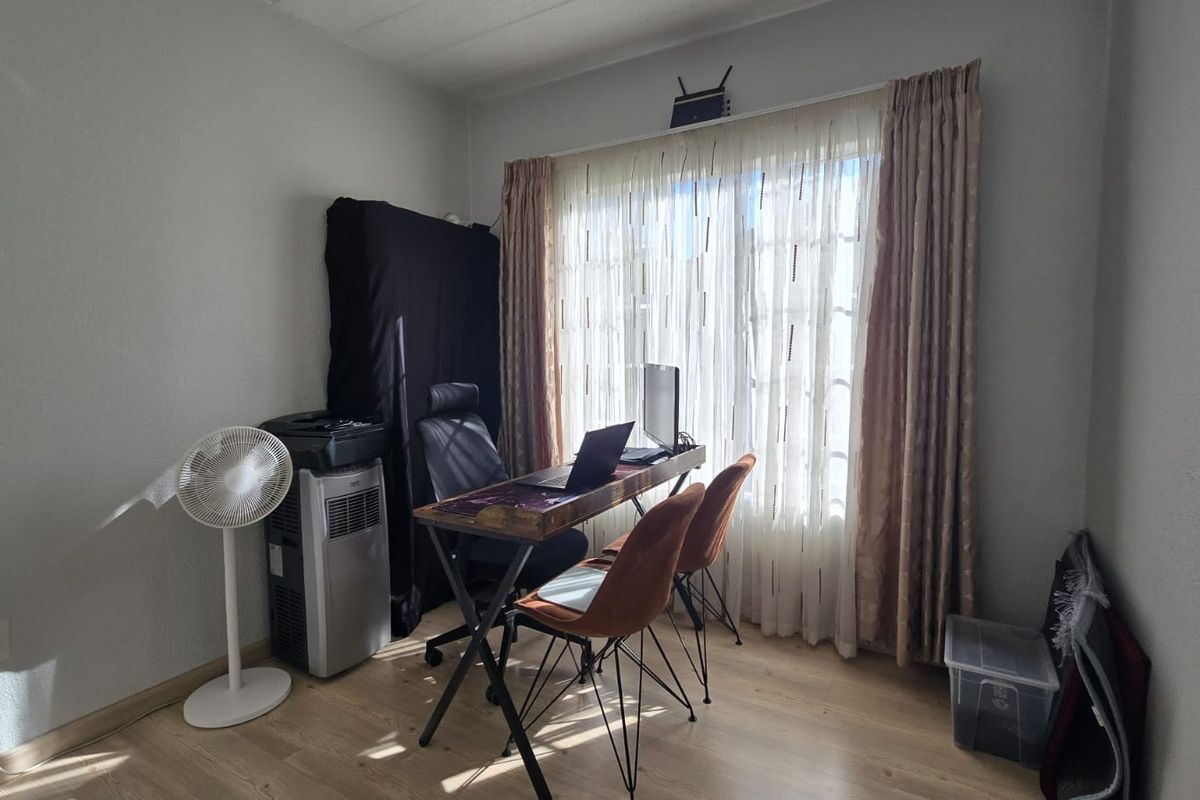 A functional bedroom space featuring laminate flooring and large windows with curtain treatments, currently utilized as a home office area.