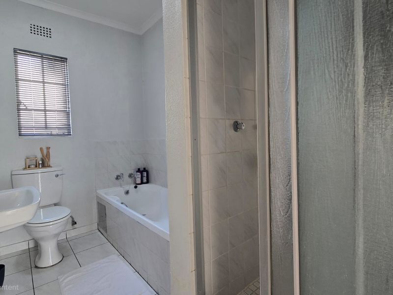 A functional bathroom featuring a pedestal basin, toilet, built-in bathtub, and a separate shower enclosure with tiled finishes.