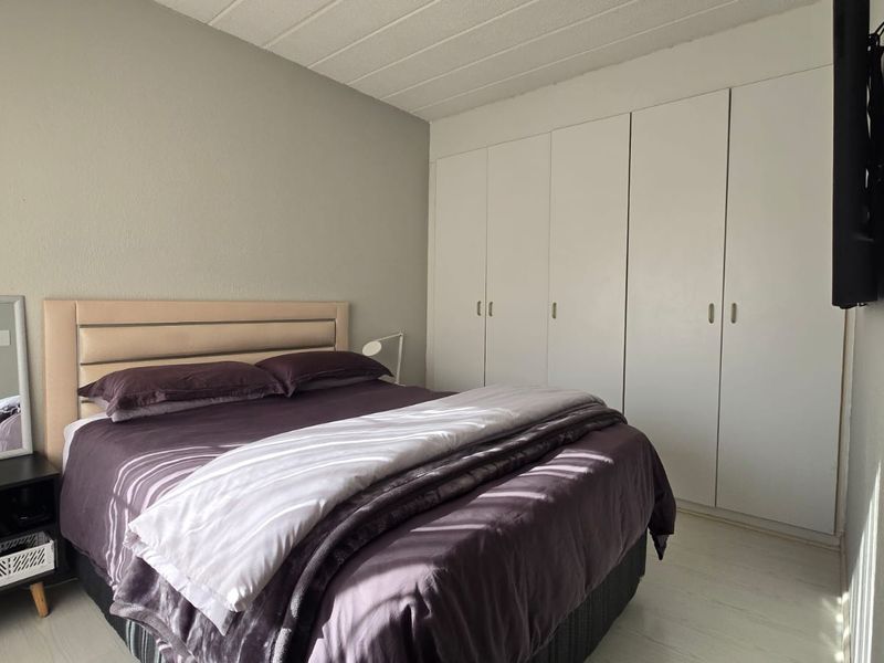 A bedroom featuring built-in cupboards and light-toned laminate flooring, offering a functional space with neutral wall finishes.