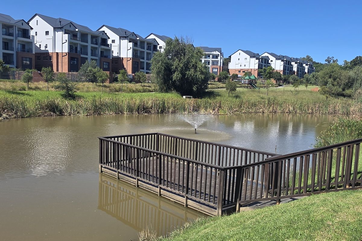 A scenic view of the apartment complex featuring a tranquil pond with a central fountain and a wooden viewing deck.