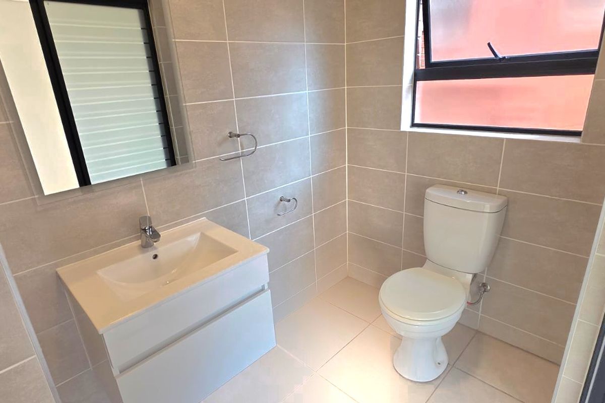 A modern, clean bathroom featuring neutral wall and floor tiles, a contemporary vanity with basin, and a standard toilet.