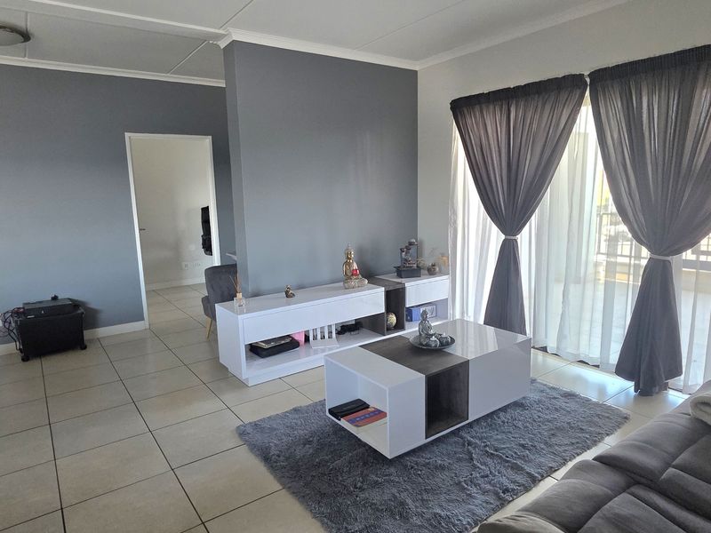 A spacious living room featuring neutral tiled flooring, a central partition wall, and large sliding glass doors providing access to an outdoor area.