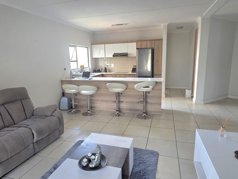 Open-plan living area featuring a modern kitchen with breakfast bar, neutral tiled flooring, and clean finishes throughout the combined space.