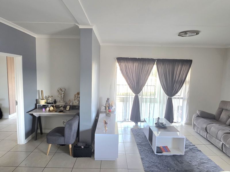 A bright living room featuring neutral tiled flooring, a feature wall, and a sliding glass door providing natural light.