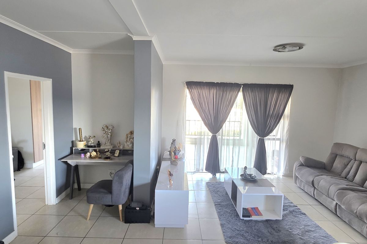 A bright living room featuring neutral tiled flooring, a feature wall, and a sliding glass door providing natural light.