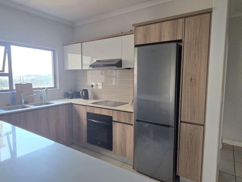 Modern kitchen featuring wood-grain cabinetry, stone countertops, integrated appliances, and a tiled backsplash, offering a clean and functional workspace.