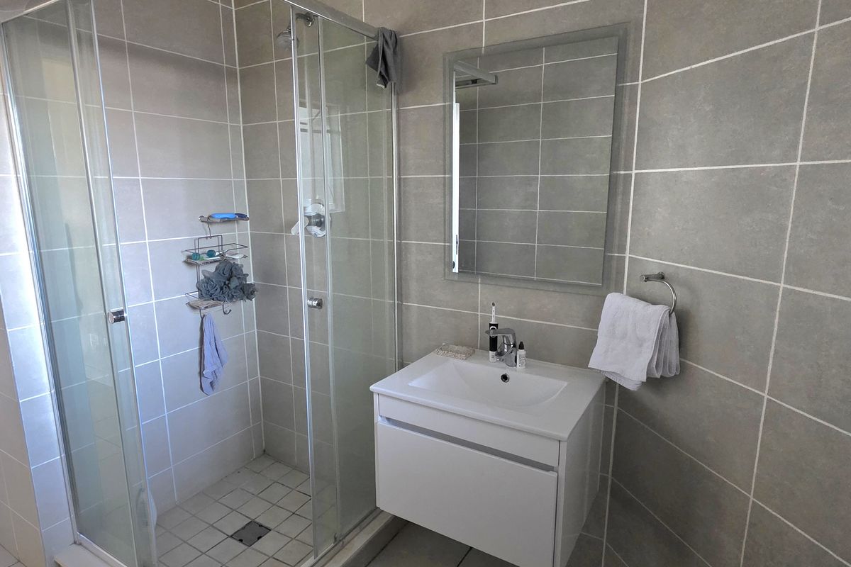 Modern bathroom featuring a glass shower enclosure, wall-mounted vanity with basin, and neutral ceramic wall tiling.