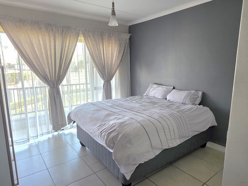 A well-lit bedroom featuring tiled flooring, a built-in cupboard, and a sliding glass door providing access to an outdoor area.