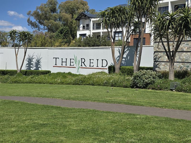 The entrance facade and landscaped grounds of The Reid townhouse complex, featuring stone-clad boundary walls and well-maintained garden areas.