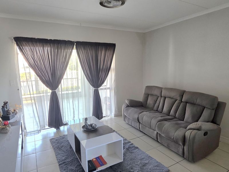 A bright and neutral living room featuring tiled flooring and a large sliding glass door that provides access to the exterior.