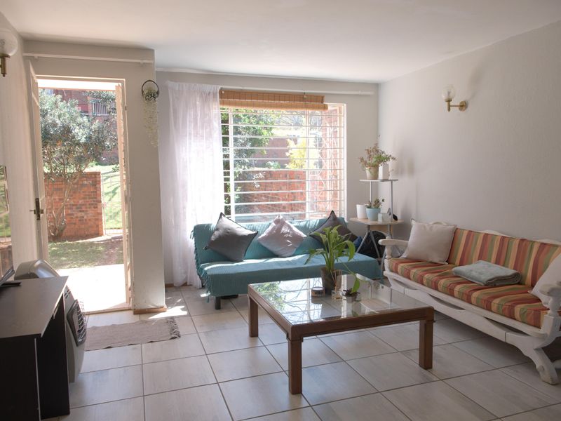 A bright living room featuring tiled flooring, wall-mounted lighting, and direct access to an outdoor area through a glass-paneled door.
