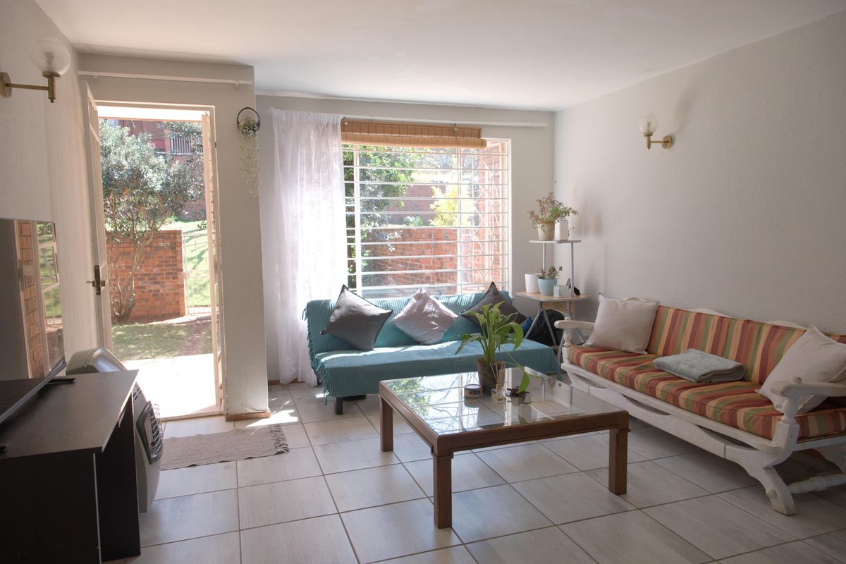 A bright living room featuring tiled flooring, wall-mounted lighting, and direct access to an outdoor area through a glass-paneled door.