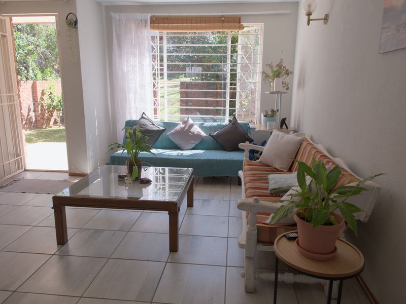 A bright living room featuring tiled flooring, security bars on the window, and direct access to an outdoor area through a security gate.