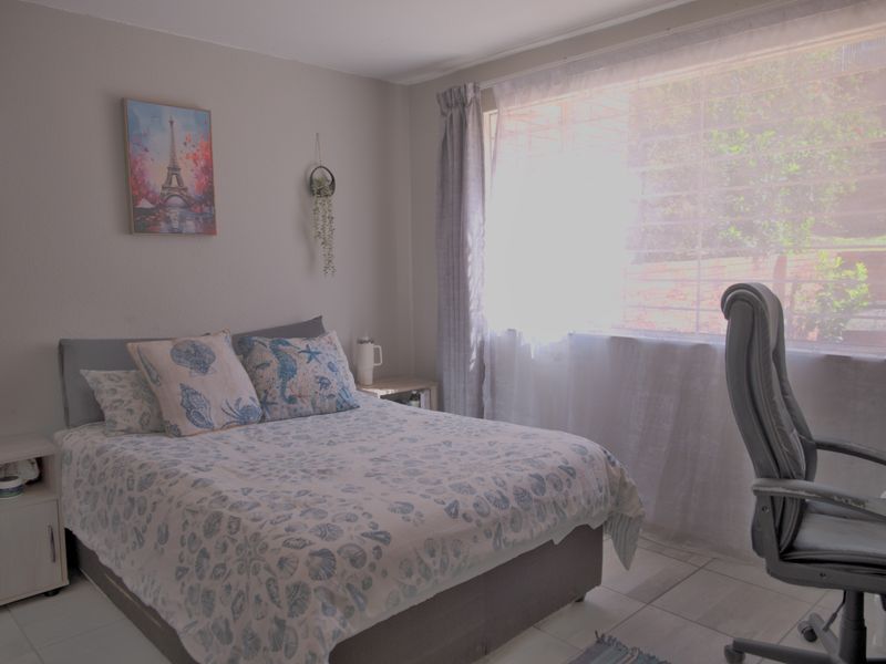 A bedroom featuring tiled flooring and a large window fitted with security bars, providing natural light.