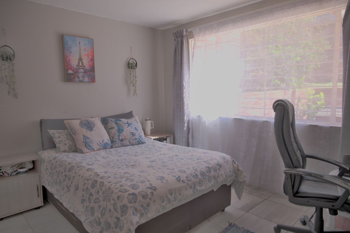 A bedroom featuring tiled flooring and a large window fitted with security bars, providing natural light.