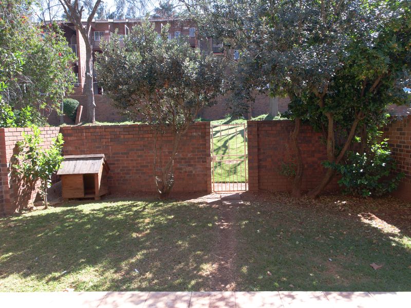 A private rear garden featuring a lawn, mature trees, and a brick boundary wall with a metal pedestrian gate.