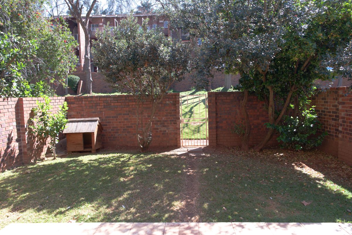 A private rear garden featuring a lawn, mature trees, and a brick boundary wall with a metal pedestrian gate.
