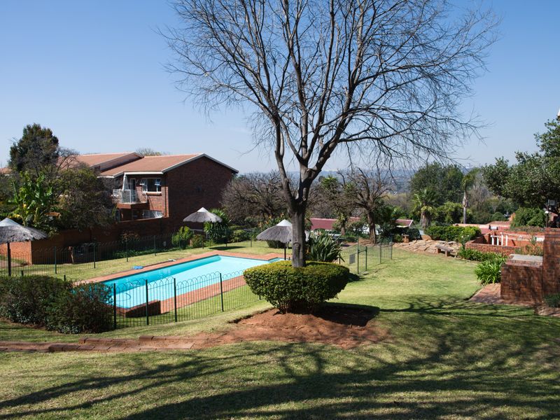 A well-maintained communal pool area featuring a swimming pool, secure fencing, and landscaped garden surroundings within the apartment complex.