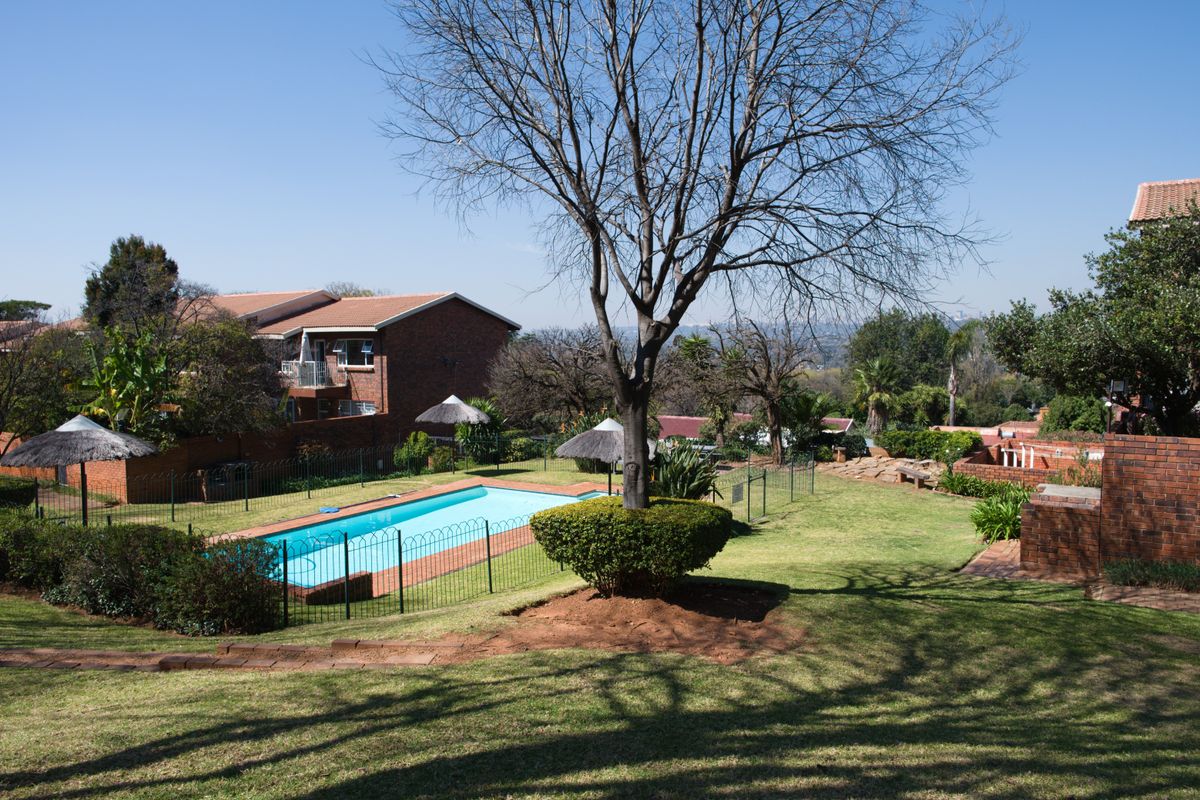 A well-maintained communal pool area featuring a swimming pool, secure fencing, and landscaped garden surroundings within the apartment complex.