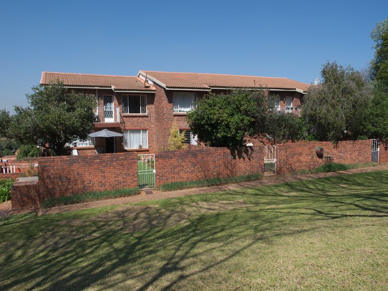 A view of the rear elevation of a face brick apartment complex featuring a private garden area enclosed by a perimeter brick wall.