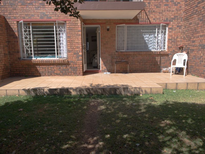 Rear view of the apartment featuring a brick facade, a tiled patio area, and a small private lawn.
