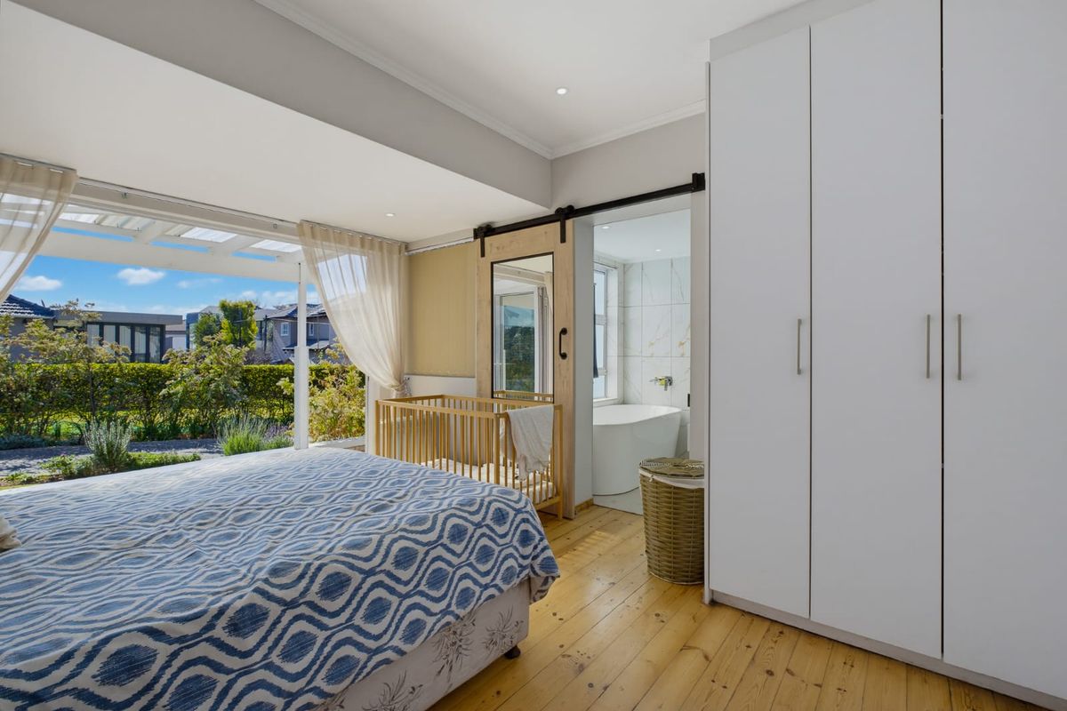 Spacious bedroom featuring hardwood flooring, built-in wardrobes, and a sliding barn door leading to an en-suite bathroom, with direct access to a garden patio.