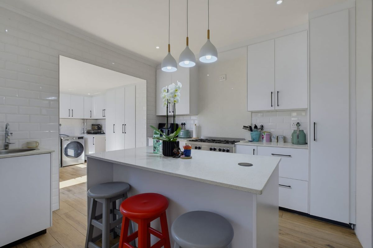 Modern kitchen featuring a central island, stone countertops, subway tile backsplash, and integrated gas hob, with an adjacent scullery area.
