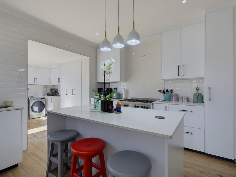 Modern kitchen featuring a central island, stone countertops, subway tile backsplash, and integrated gas hob, with an adjacent scullery area.