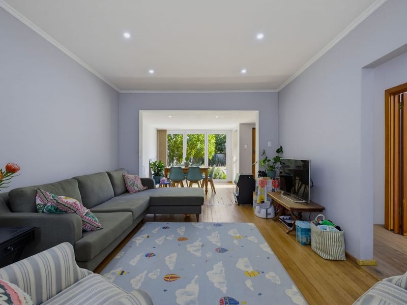 An open-plan living and dining area featuring hardwood flooring, recessed downlighting, and large glass doors providing natural light and garden access.
