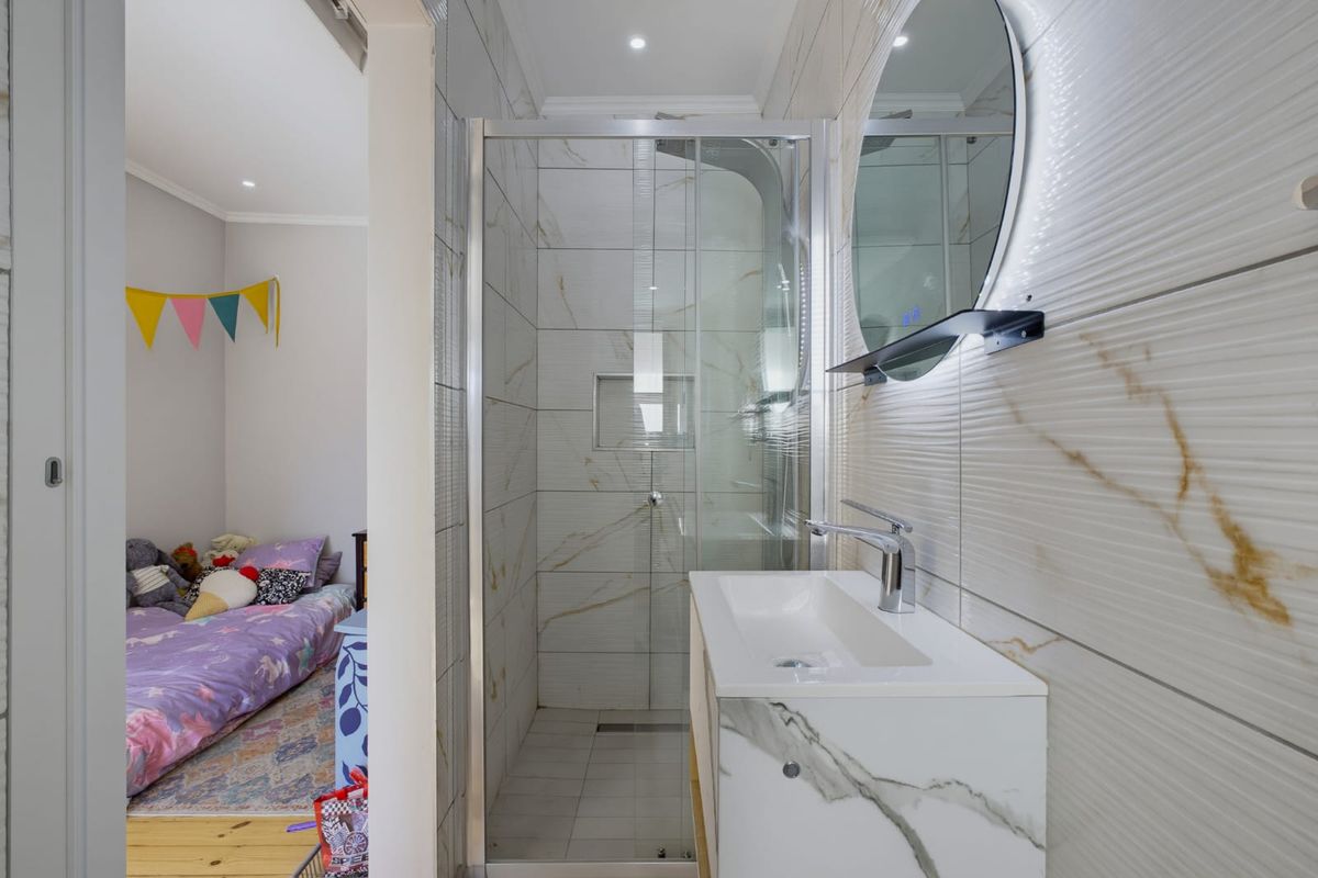 Modern bathroom featuring a walk-in shower with glass enclosure, marble-look wall tiles, and a contemporary vanity with an integrated basin and LED mirror.