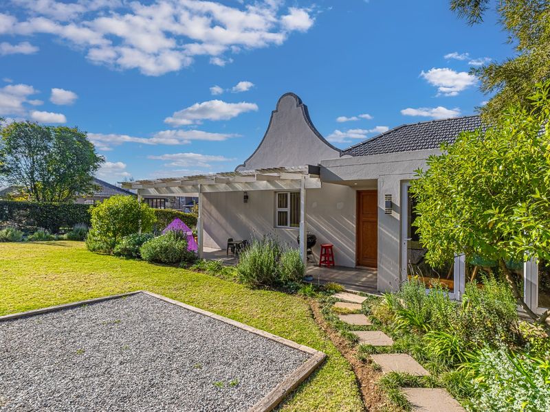 Rear view of the property featuring a covered patio with a pergola, a well-maintained garden, stone pathway, and a gravel area.