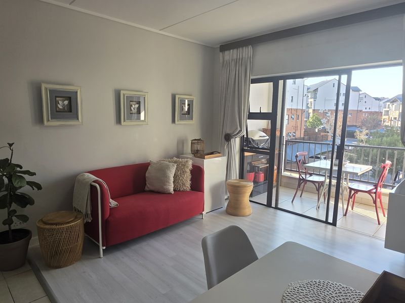 A bright living room featuring light-toned laminate flooring and a large sliding glass door that provides access to a private balcony.