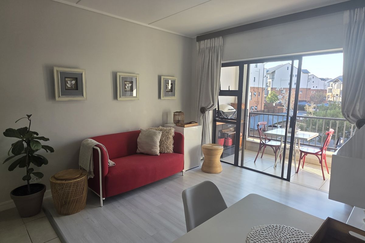 A bright living room featuring light-toned laminate flooring and a large sliding glass door that provides access to a private balcony.