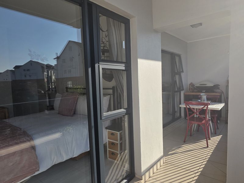 A covered balcony featuring tiled flooring, metal balustrades, and large sliding glass doors providing access to the interior bedroom.