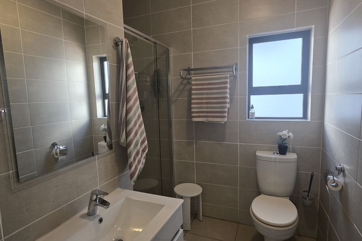 A modern, well-maintained bathroom featuring neutral wall tiles, a glass shower enclosure, a vanity basin, and a toilet.