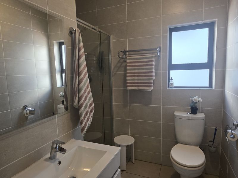 A modern, well-maintained bathroom featuring neutral wall tiles, a glass shower enclosure, a vanity basin, and a toilet.