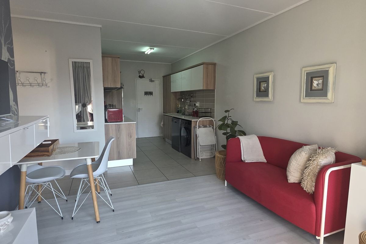 Open-plan living area featuring a combined lounge and kitchen space with laminate flooring, tiled kitchen zone, and built-in cabinetry.