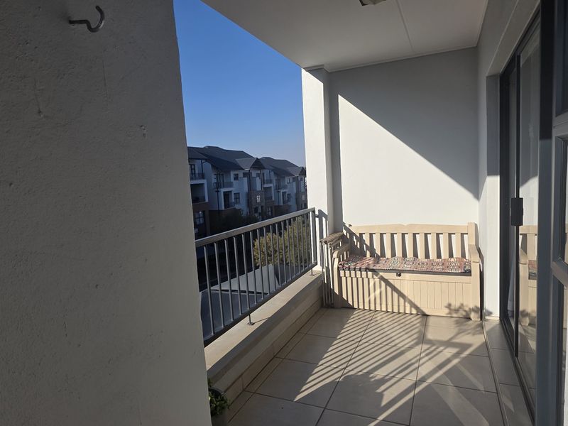 A covered balcony featuring tiled flooring and a metal balustrade, providing an outdoor space accessible through sliding glass doors.