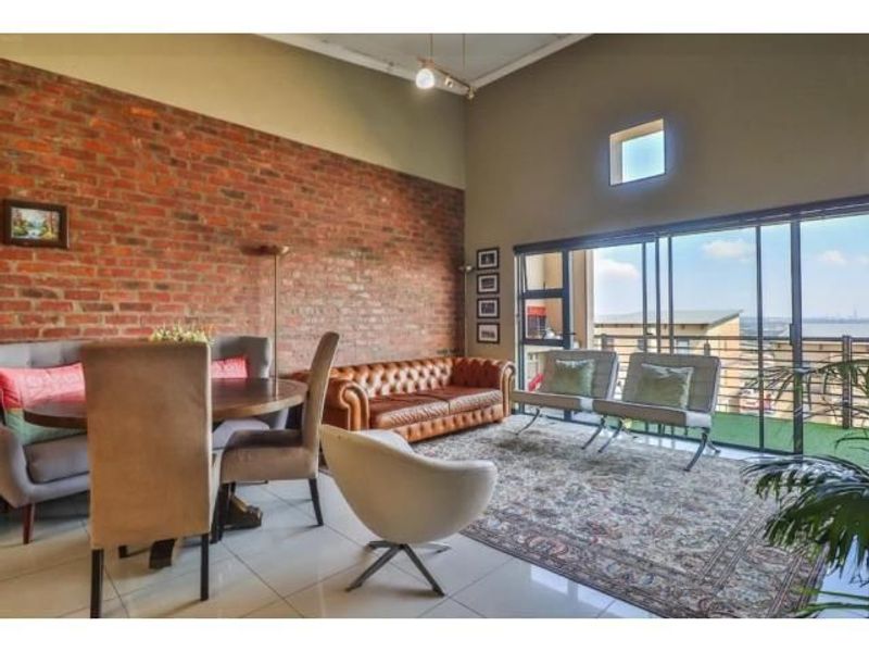 Spacious living area featuring an exposed brick feature wall, high ceilings, and large sliding glass doors that provide ample natural light and outdoor access.