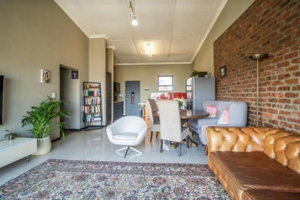 Spacious open-plan living and dining area featuring an exposed brick feature wall, tiled flooring, and a modern kitchen layout.