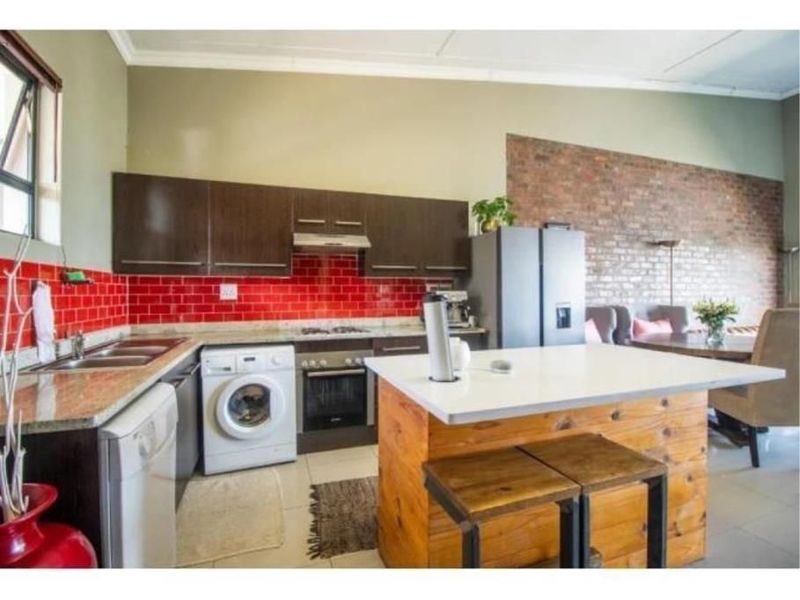 Open-plan kitchen featuring dark cabinetry, granite countertops, a red subway tile backsplash, and a central island, seamlessly flowing into the living area.