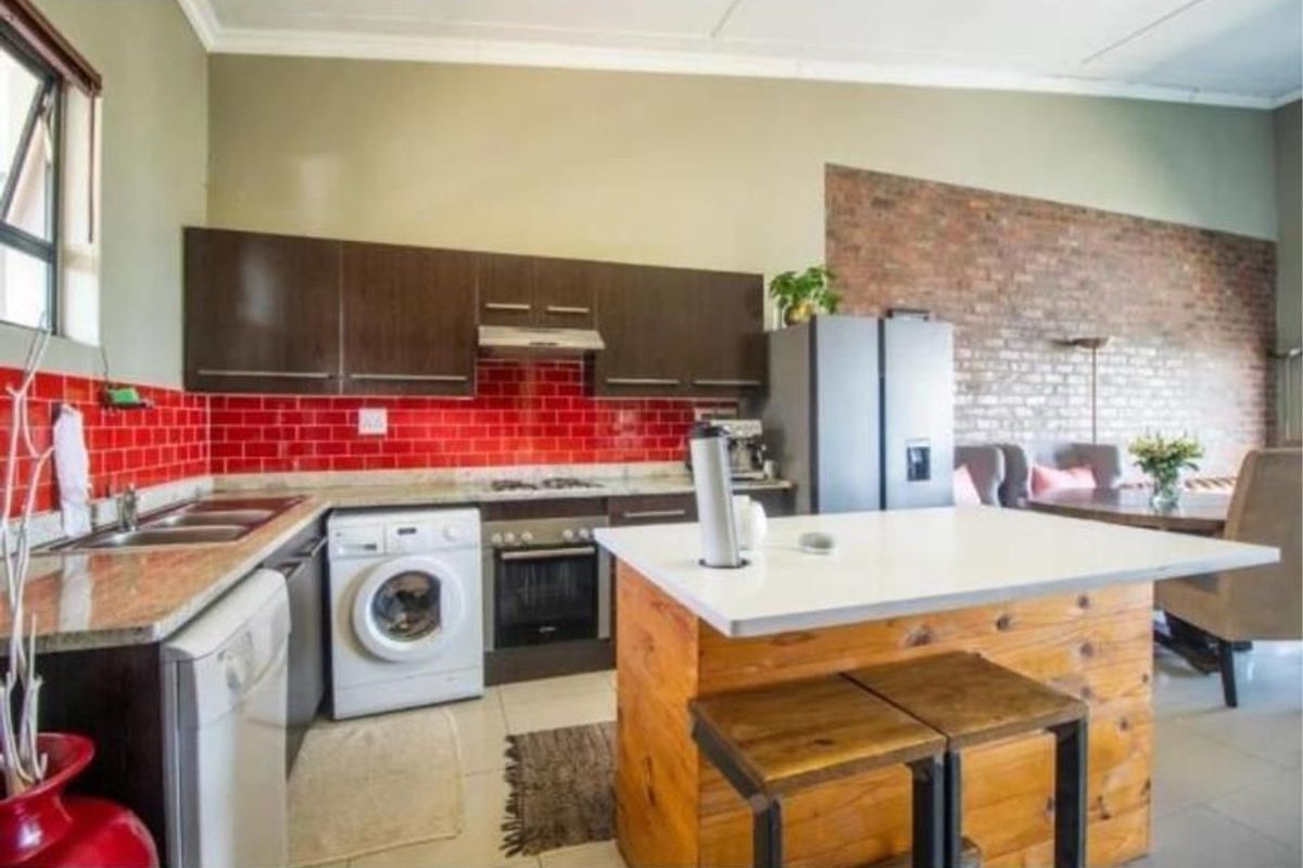 Open-plan kitchen featuring dark cabinetry, granite countertops, a red subway tile backsplash, and a central island, seamlessly flowing into the living area.
