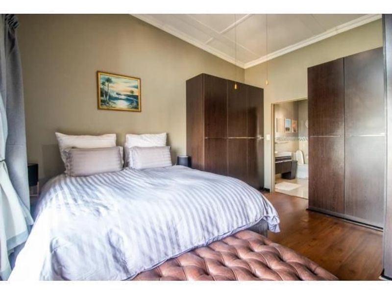 A well-maintained bedroom featuring built-in cupboards, laminate flooring, and a coffered ceiling, with an adjoining en-suite bathroom visible.