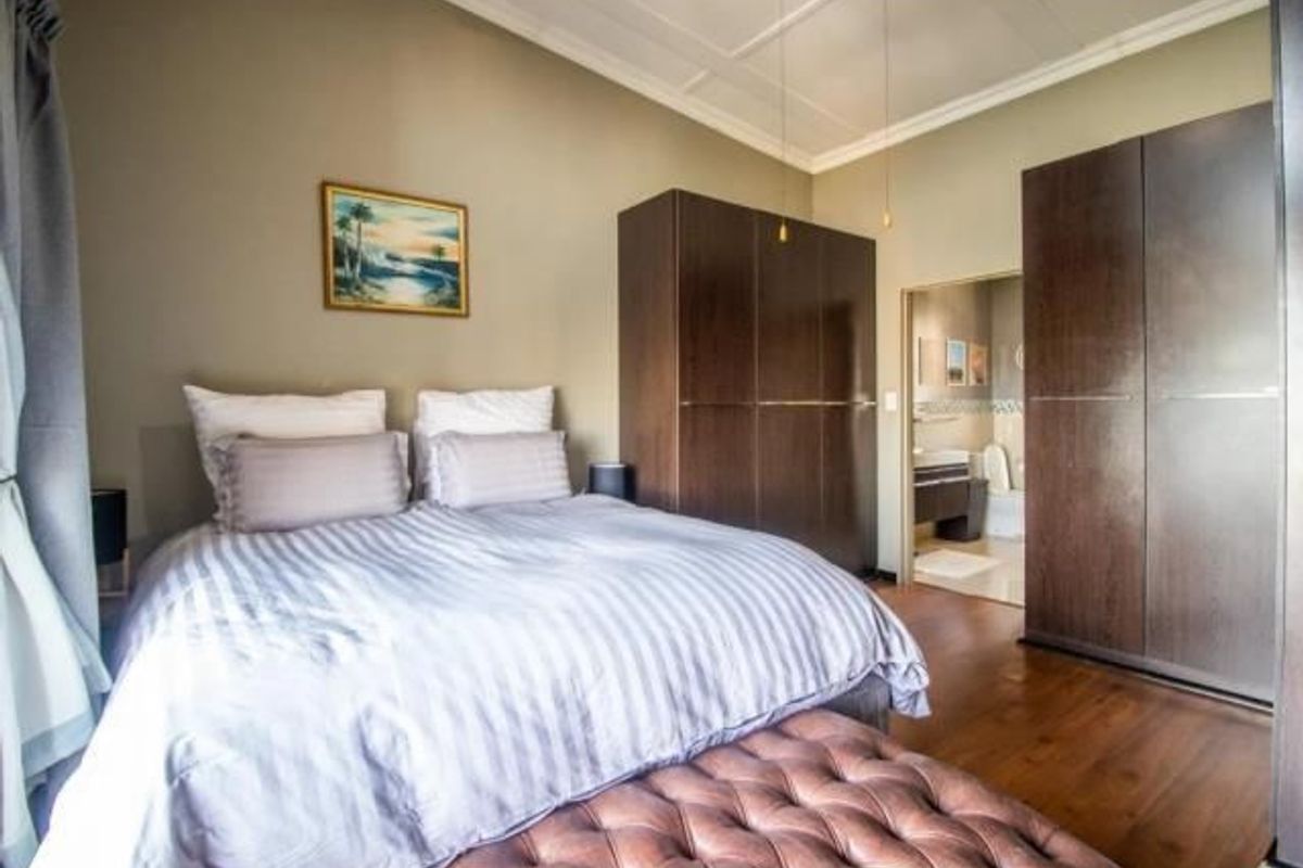 A well-maintained bedroom featuring built-in cupboards, laminate flooring, and a coffered ceiling, with an adjoining en-suite bathroom visible.