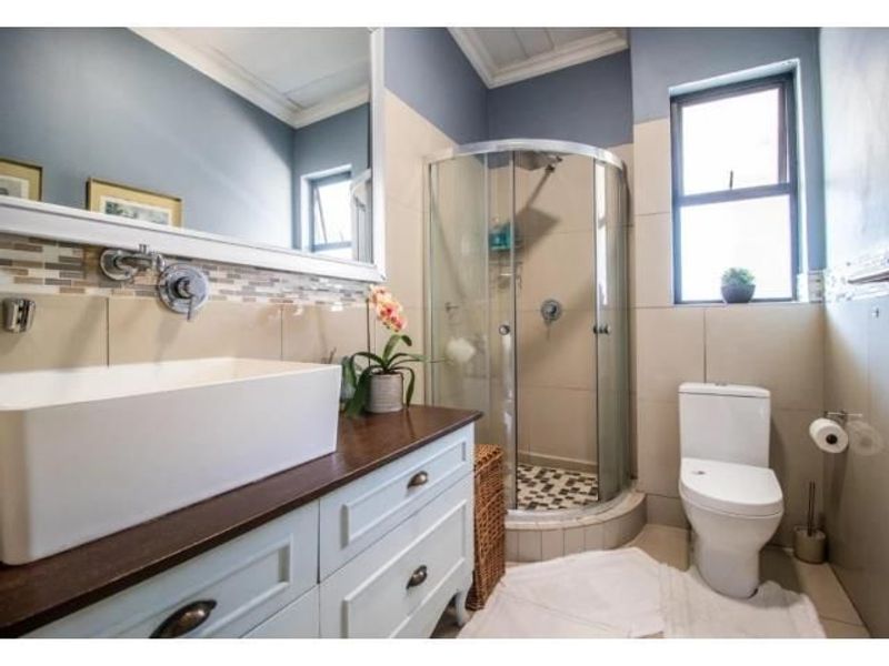 A well-maintained bathroom featuring a modern vessel sink on a vanity cabinet, a corner shower enclosure, and a toilet with neutral wall tiling.