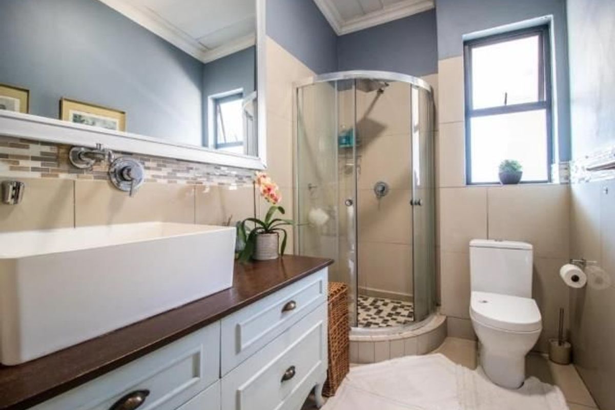 A well-maintained bathroom featuring a modern vessel sink on a vanity cabinet, a corner shower enclosure, and a toilet with neutral wall tiling.