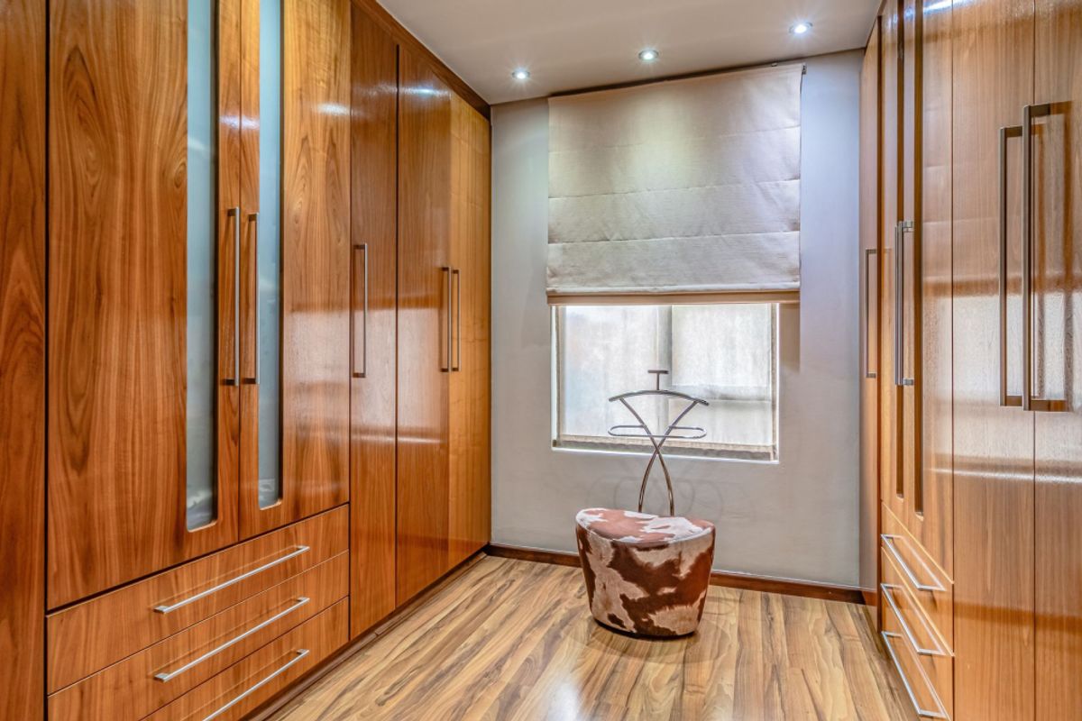 A well-appointed dressing room or bedroom featuring extensive floor-to-ceiling built-in wooden cabinetry, laminate flooring, and recessed lighting.