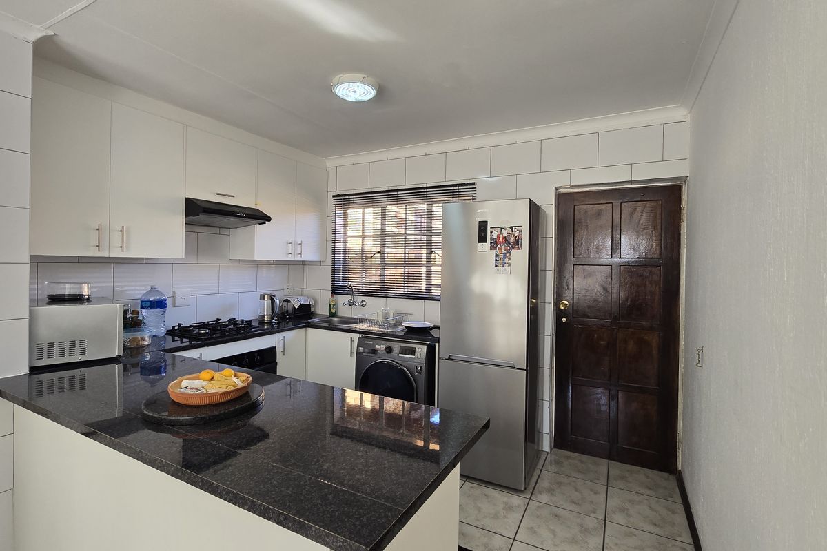 Functional kitchen featuring granite countertops, white cabinetry, gas hob, extractor fan, and tiled finishes with direct access to an exterior door.