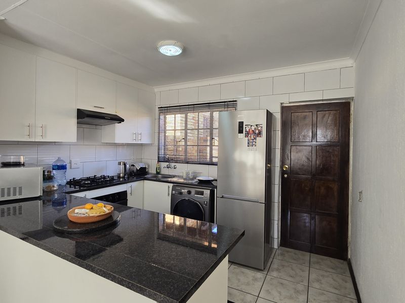 Functional kitchen featuring granite countertops, white cabinetry, gas hob, extractor fan, and tiled finishes with direct access to an exterior door.